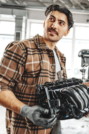Man works on car engine part in garage during daytime with natural light coming through windowsの写真素材