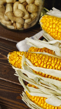 Fresh corn on the cob with husks placed beside a jar of peanuts indoorsの写真素材