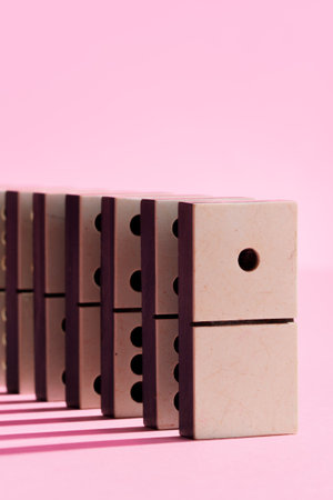 Stacked dominoes fall in a line against a bright pink background during a playful activityの写真素材