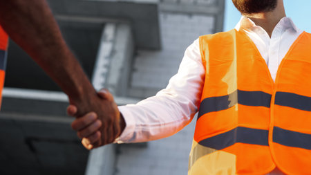Workers shake hands at a construction site during daylight hours in a city
