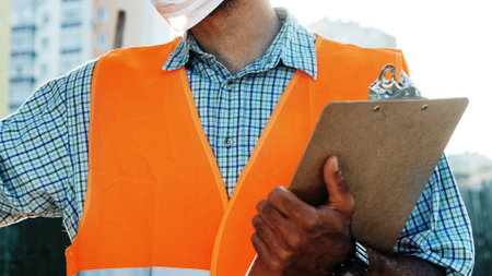 Worker checks construction site details while holding clipboard in city setting during daytimeの写真素材