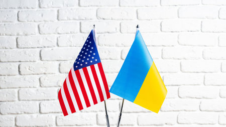 Flags of the United States and Ukraine stand together against a white brick wallの写真素材