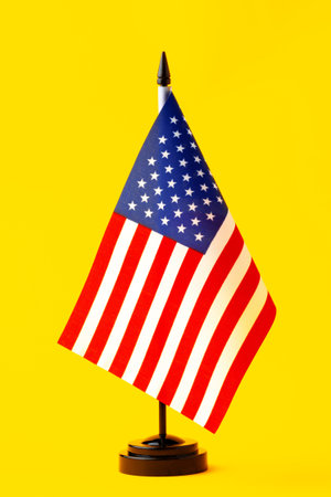 Small American flag on a black base against a bright yellow backgroundの写真素材