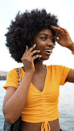 Woman talking on the phone near the water while enjoying a sunny dayの写真素材