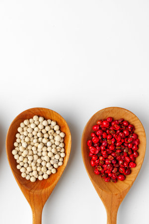 Different types of pepper in wooden spoons on a white background