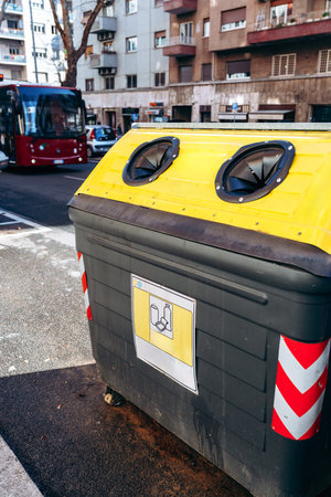 Modern recycling bin on city street near buildings and bus in daytime