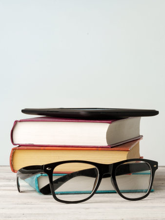 Stack of books with glasses and a notebook on a wooden table in a quiet room setting