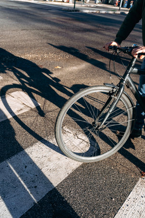 Biker stops at crosswalk during midday in a city street with shadows cast on pavement