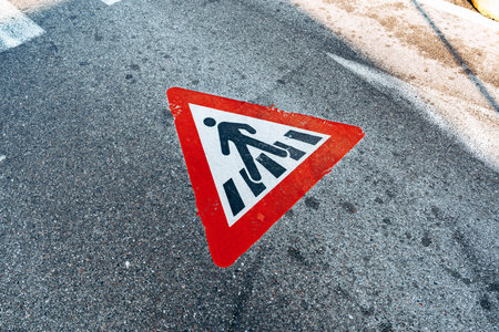 Warning sign for pedestrian crossing on road surface in urban area during daytime