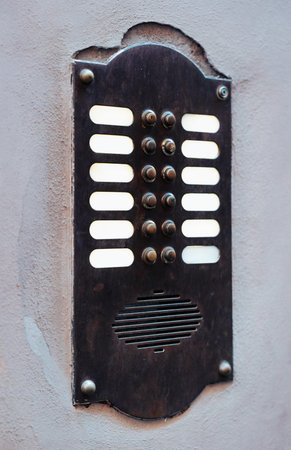 Old metal intercom panel on wall in urban setting with many buttons present