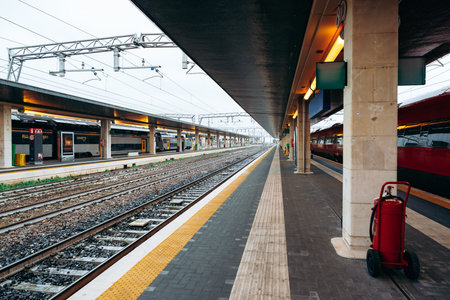 Train station platform with tracks and waiting area during a cloudy dayの写真素材