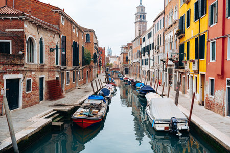 Quiet canal in Venice with boats and colorful buildings in the background near evening sky