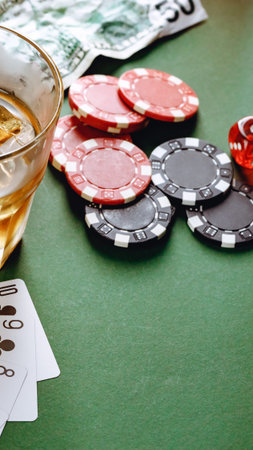 Set of poker chips lies beside a glass of whiskey and playing cards on a green table