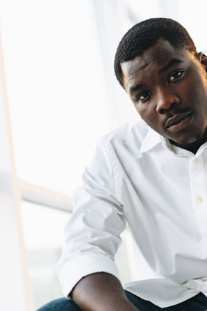 Young man sits indoors, looking at the camera in a bright setting