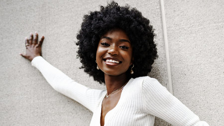 Woman smiles brightly while leaning against a wall in a casual indoor settingの写真素材