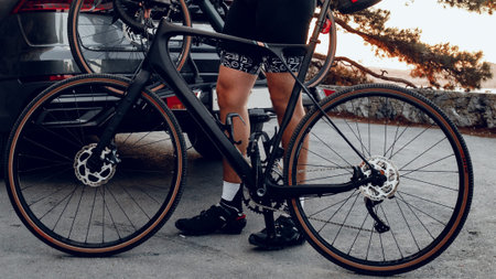 Biker prepares for a ride by a dark car at sunset in a parking area by trees