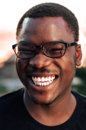 Man smiles widely while wearing glasses during sunset in outdoor settingの写真素材