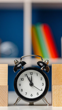 Clock sits on a table between wooden blocks and colorful books in a roomの写真素材