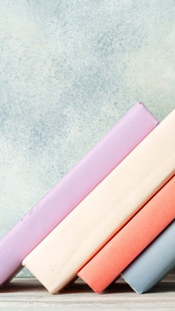 Colorful stacked books resting on a wooden shelf against a blue wall