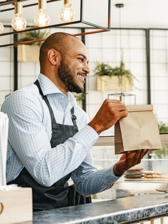 Barista hands coffee bag to customer in a busy cafe during afternoon rush
