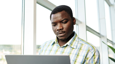 Man works on laptop near window in modern office building during daylight hours