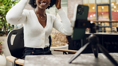 Young woman smiles while adjusting hair during video call at a cafe in the afternoonの写真素材