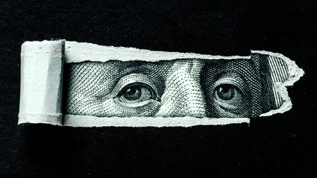 Dollar currency showing a close-up view of a face peeking through torn paper in a simple setting
