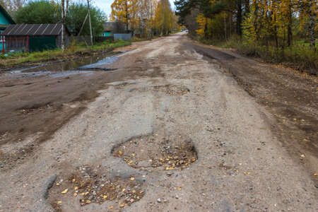 Bad road in the village, holes, hollows. The road to the village is very poorly repaired, the pits appear constantly.の写真素材