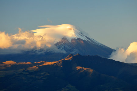 The imposing Cotopaxi volcano, shrouded in clouds and with its snow-capped summit, is revealed in a sunrise captured from the cable car in Quito, Ecuador. The scene combines the natural grandeur of the Andes with the serenity of the first light of day, offering a unique moment that highlights the connection between volcanic majesty and the traveler's experience.の写真素材
