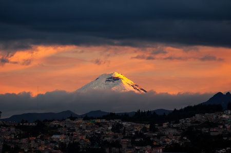 Striking image capturing the majesty of the Cotopaxi Volcano at dusk. In the foreground, a portion of the city of Quito can be seen, its lights just beginning to turn on.の写真素材