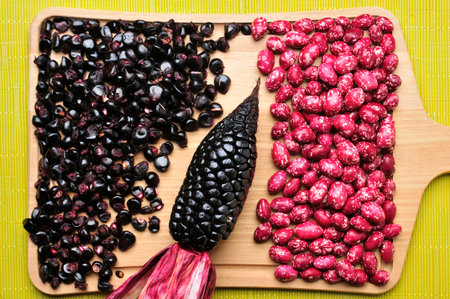 Vibrant overhead shot featuring black corn, shelled corn kernels, and pink beans with white flecks, all arranged on a light-colored wooden cutting board. This image evokes the richness of natural and healthy ingredients.の写真素材