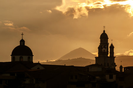 The golden silhouette of the SangolquÃ­ church and its surroundings stands out against a dramatic sunset sky.の写真素材