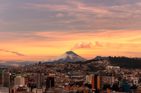 Stunning cityscape of Quito, Ecuador, under a golden sky at sunset. The imposing Cotopaxi Volcano rises on the horizon, emitting a plume of smoke.の写真素材