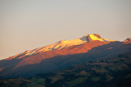 A majestic sunrise illuminates the snow-capped summit of the Guagua Pichincha Volcano with golden light.の写真素材