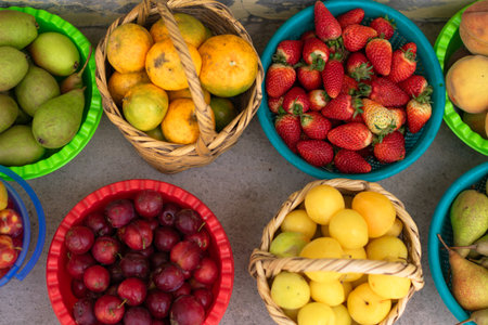 Top view of colorful baskets filled with a variety of fresh fruits such as strawberries, pears, and plums at a market. A vibrant scene representing abundance, healthy eating, and local commerce.の写真素材