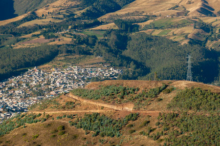 Aerial view capturing the transition from city to nature, with an electrical tower on a hill, connecting a peripheral neighborhood with a landscape of Andean mountains and fields.の写真素材
