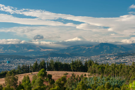 Spectacular panoramic view of Quito from Casitagua, Ecuador, capturing the urban sprawl surrounded by Andean forests and majestic mountains, under a blue sky with white clouds.の写真素材