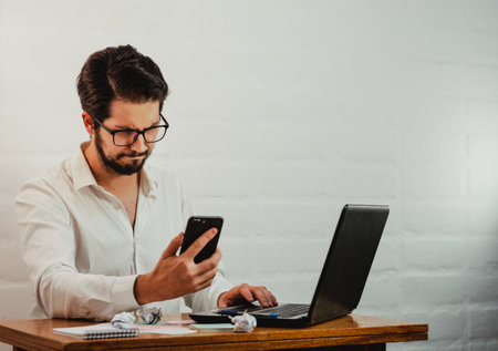 Latin man in glasses working. Using laptop and cell phone. Work at home concept. Copy space.の写真素材