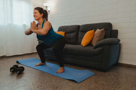 Vertical shot of a pregnant Latina woman stretching after yoga and exercise. Concept of healthy life during pregnancy and exercise at home.の写真素材