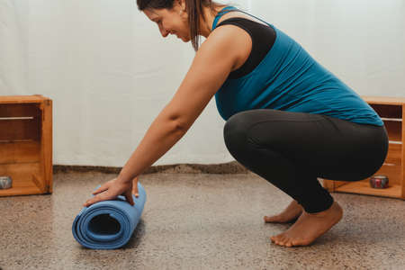 Vertical shot of a pregnant Latina woman stretching after yoga and exercise. Concept of healthy life during pregnancy and exercise at home.の写真素材