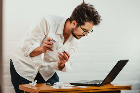 Young man standing pointing a pen at the notebook screen. Close up action. Home Office.の写真素材
