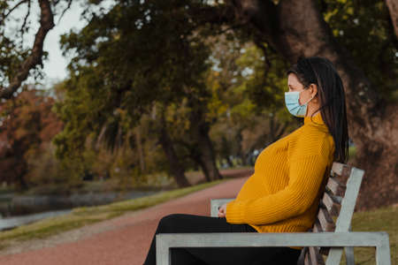 Horizontal shot of a Latina woman in a mask standing alone outside, looking into the distance. Outdoors concept in times . Copy spaceの写真素材