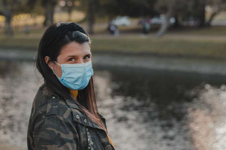 Horizontal shot of a Latina woman in a mask standing alone outside, looking into the distance. Outdoors concept in times . Copy spaceの写真素材