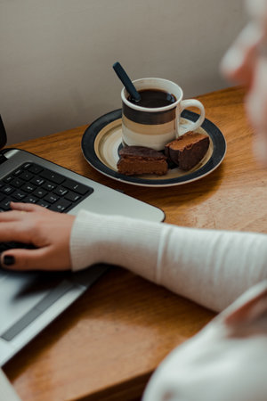Latin woman using the notebook while enjoying a cup of coffee and an alfajor, a typical candy from Uruguay and Argentina.の写真素材