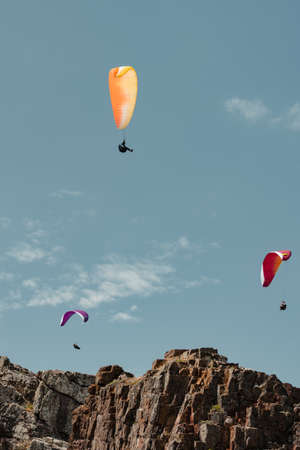 Three paragliders forming a triangle while gliding over a cliffの写真素材