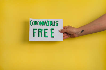 A closeup shot of a woman holding a paper with the word "DON'T STAY AT HOME" on a yellow backgroundの写真素材