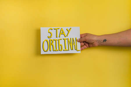 A closeup shot of a woman holding a paper with the word "DON'T STAY AT HOME" on a yellow backgroundの写真素材