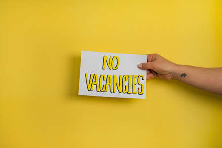 A closeup shot of a woman holding a paper with the word "DON'T STAY AT HOME" on a yellow backgroundの写真素材