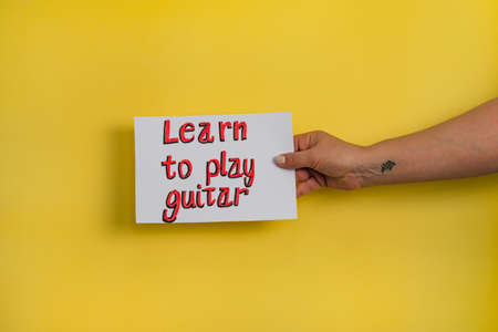 A closeup shot of a woman holding a paper with the word "LEARN TO PLAY GUITAR" on a yellow backgroundの写真素材