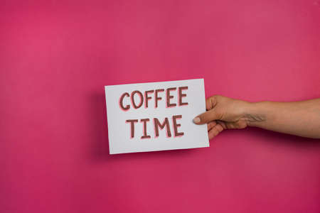 A closeup shot of a woman holding a paper with the word COFFEE TIME on a fuchsia background